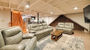 A spacious living area with a high ceiling, a wooden staircase, a kitchen in the background, and a large TV mounted on the wall. - Red River Gorge Cabin: Hike + Relax! (Rogers)