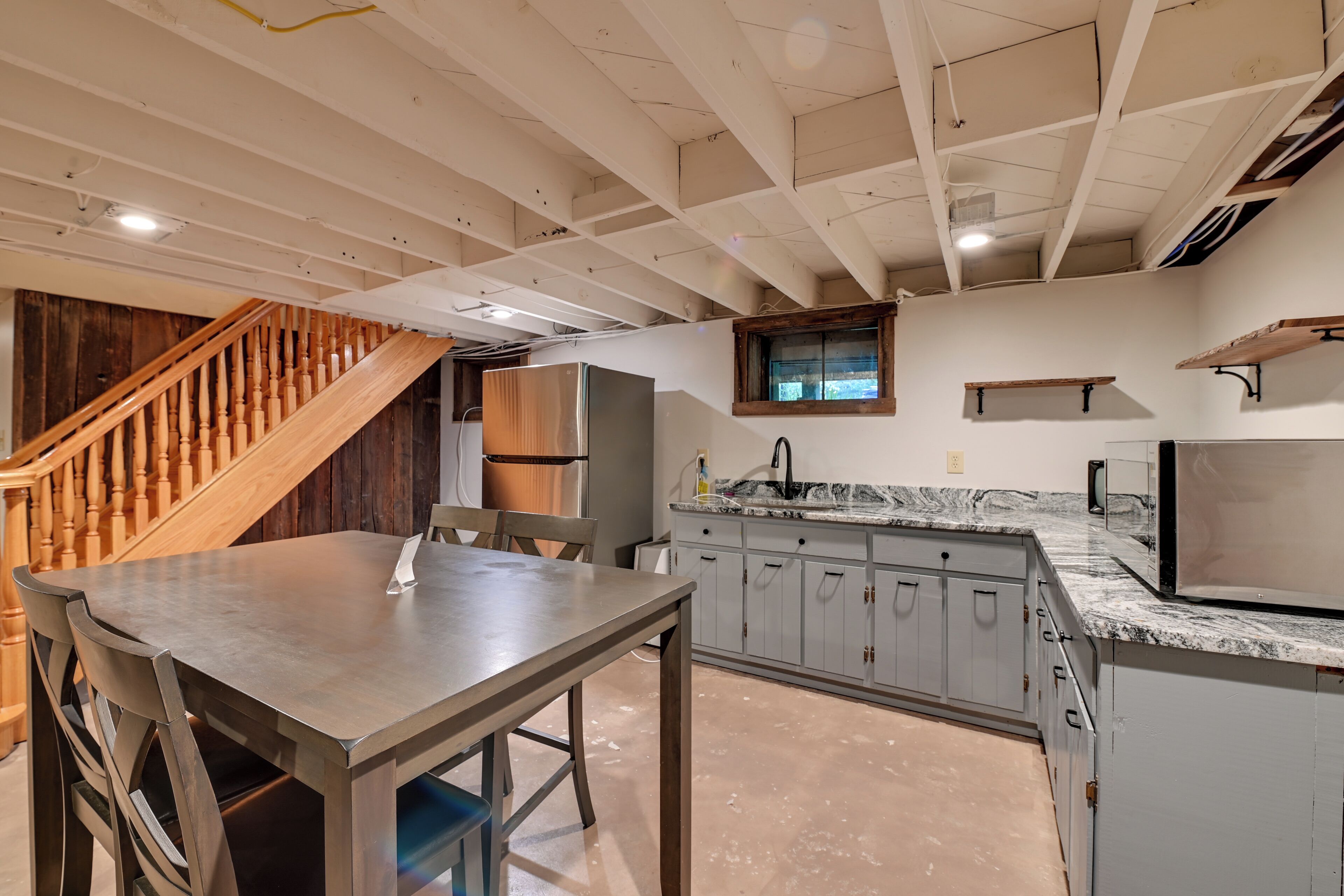 A kitchen with a wooden staircase, granite countertops, and a stainless steel refrigerator.