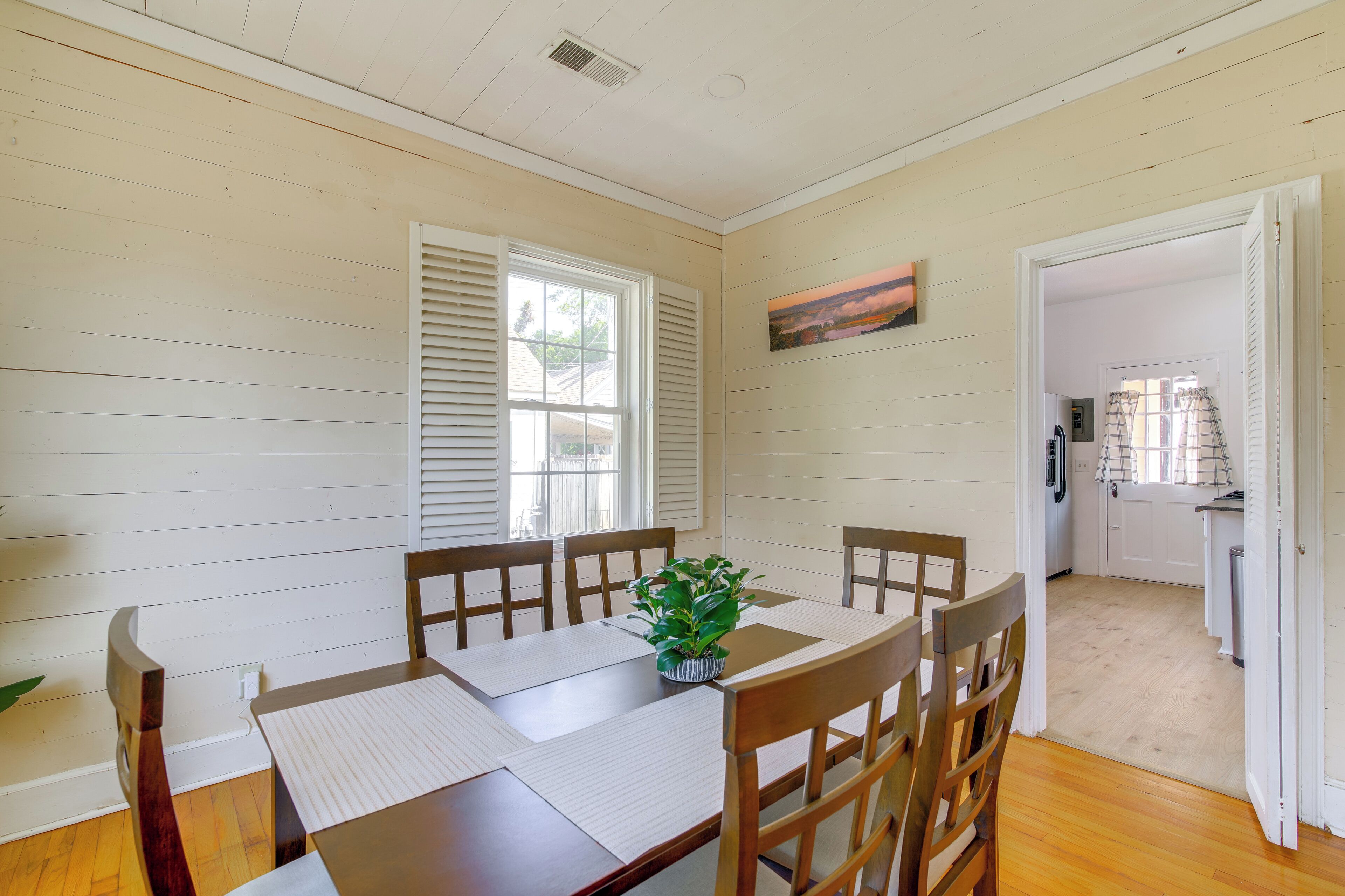 A dining area with a wooden table and chairs, a potted plant, and a painting on the wall.