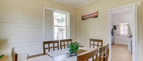 A dining area with a wooden table and chairs, a potted plant, and a painting on the wall.