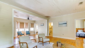 Ein geräumiges Wohnzimmer mit Holzböden, zwei helle Sofas, einem runden Couchtisch und einem Deckenventilator.