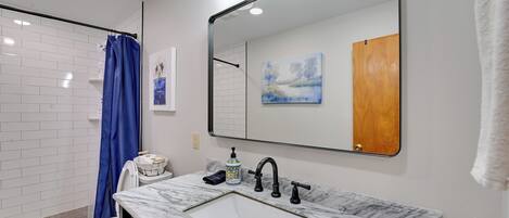 A bathroom with a white sink, black faucets, a blue shower curtain, and a large mirror.