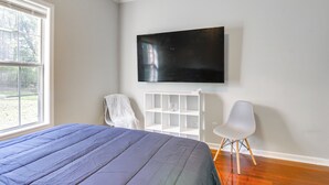 Un dormitorio con una cama, televisión montada en la pared, un estante blanco y una silla.