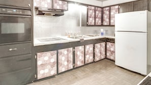 Eine Küche mit dunklen Schränken, einem weißen Kühlschrank, einer Edelstahl-Spüle und einer Mikrowelle.