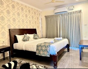 A neatly made bed with a wooden headboard, a bedside table, and a patterned wall. - Deep International Goa (Mandrem)