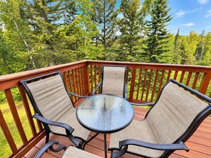 A deck with a round glass table and four chairs, surrounded by a wooden railing.