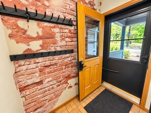 Uma porta com moldura de madeira e painel preto, um porta-roupas de metal preto e uma parede de tijolos com tinta descascada.