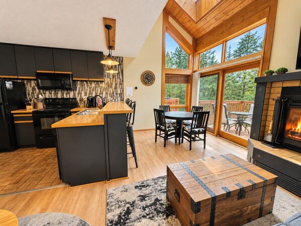 A modern kitchen with a central island, dining area with chairs, and a fireplace.