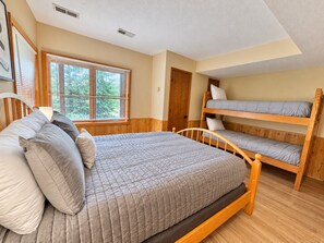 Een kamer met een enkel bed, een stapelbed, houten vloeren, een raam met zonwering en een deur.