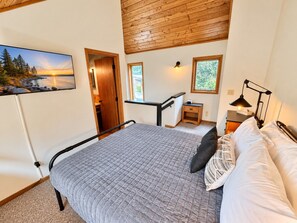 A bedroom with a bed, a desk, a chair, a nightstand, and a wall-mounted TV.