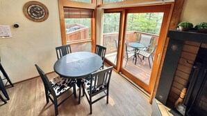 Un terrazzo in legno con tavolo e sedie rotonde, un caminetto e vista su un'altra terrazza con mobili da esterno.