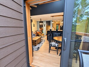 Une porte coulissante donne sur un espace repas comprenant une table et des chaises en bois, un canapé et un tapis.