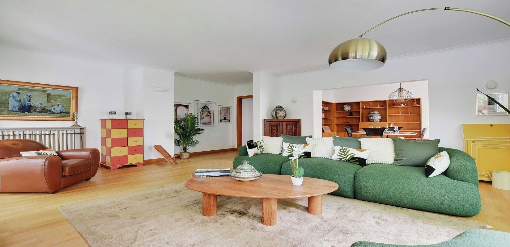 Ein Wohnzimmer mit einem grünen Sofa, einem braunen Ledersessel, einem Holztisch und einem roten und gelben Schrank.
