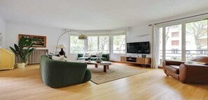 A modern living room with a green sofa, a brown leather armchair, a coffee table, and a TV on a wooden cabinet.