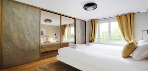 A modern bedroom with a large bed, a mirror, and a view of greenery outside.