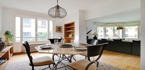 A dining area with a table set for four, surrounded by chairs, a pendant light, and a bookshelf.