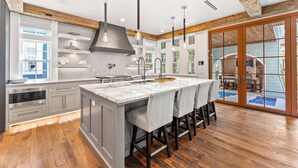 A modern kitchen with a large island, wooden beams, and a view of an outdoor patio. - Tranquility|Private Community Beach Access|Pool|Golf Cart|Game Room (WaterSound)