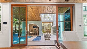 A spacious room with a wooden floor, a dining table, and a view of an outdoor patio with a pool and seating area. - Tranquility|Private Community Beach Access|Pool|Golf Cart|Game Room (WaterSound)