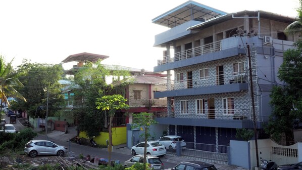 A multi-story residential building with balconies, a gated entrance, and a street view with parked cars and vegetation. - Haven Garden Homestay (Port Blair)
