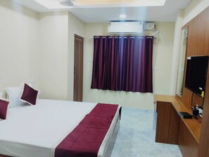 A hotel room with a bed, a desk, a television, and an air conditioning unit. - Haven Garden Homestay (Port Blair)