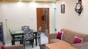 A living room with a sofa, a coffee table, and a dining table with chairs. There is a door leading to another room. - Haven Garden Homestay (Port Blair)