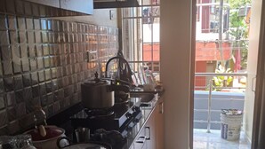 A kitchen with a tiled backsplash, stainless steel appliances, and a view of the street outside. - Haven Garden Homestay (Port Blair)