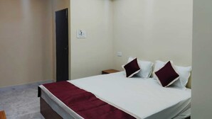 A bedroom with a bed, a nightstand, a red throw blanket, and a ceiling light fixture. - Haven Garden Homestay (Port Blair)