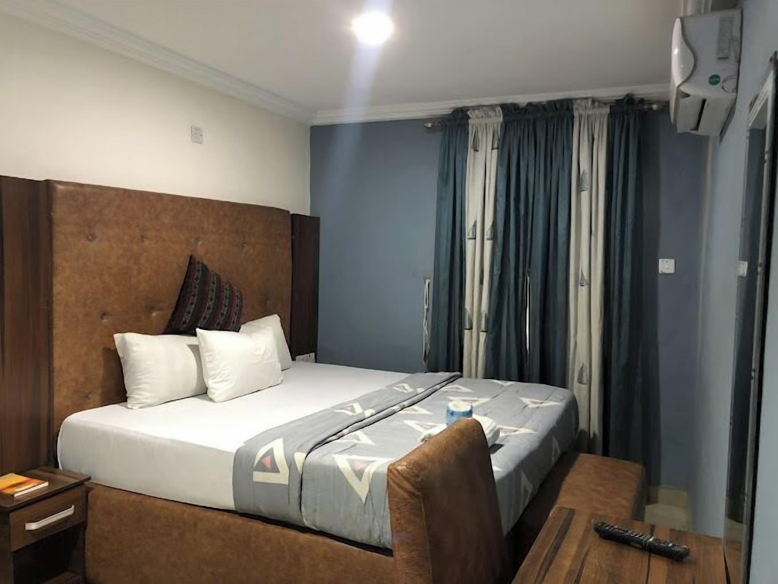 A hotel room with a large bed, a wooden headboard, a bedside table, and a desk with a chair.