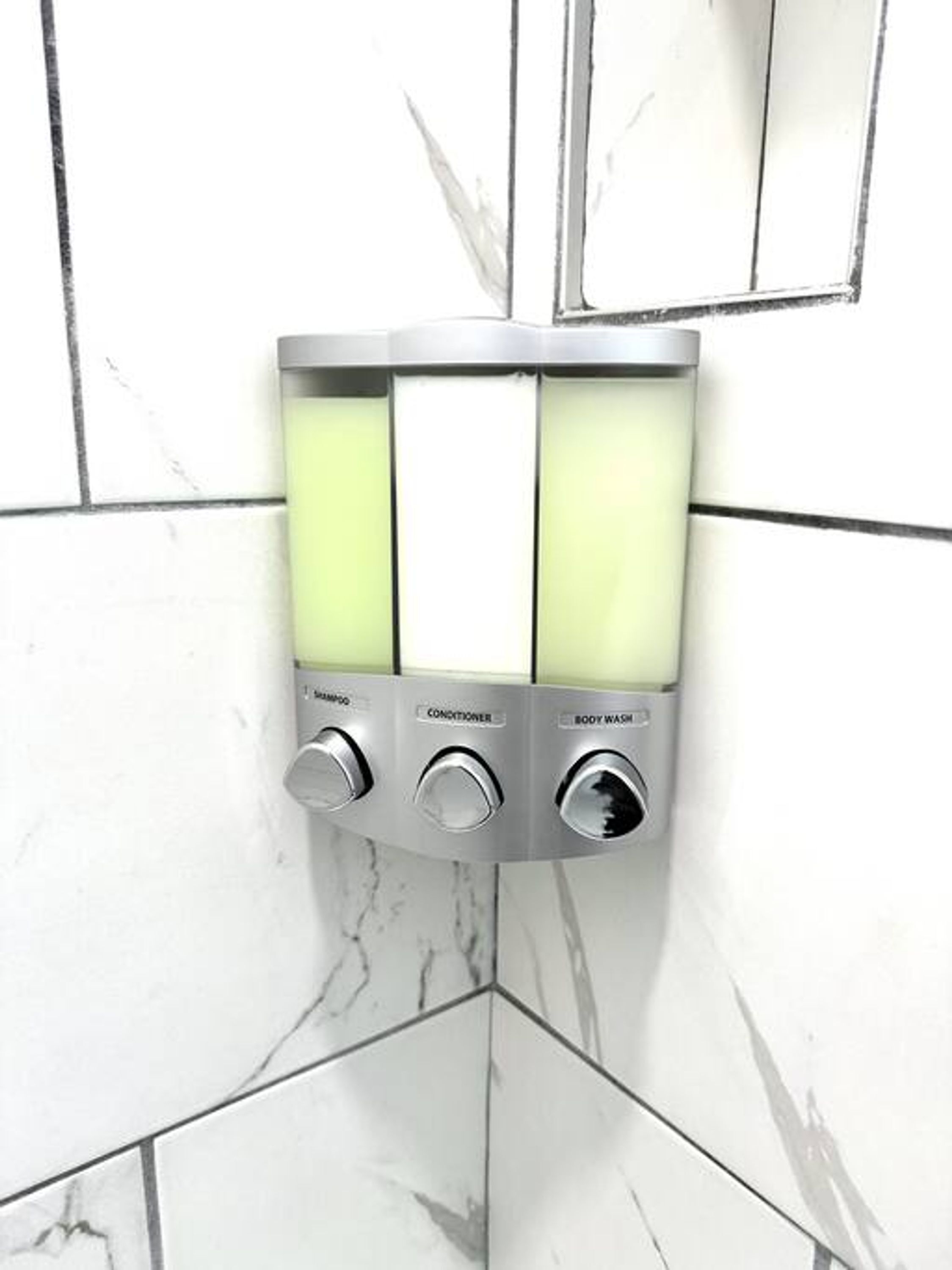 A wall-mounted soap dispenser with three sections labeled for shampoo, conditioner, and body wash.
