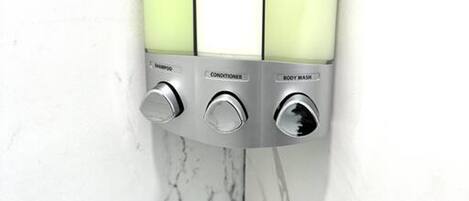 A wall-mounted soap dispenser with three sections labeled for shampoo, conditioner, and body wash.