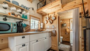 A compact kitchen with white cabinets, a teal microwave, and a hanging pot rack. - Glamping Under the Stars | Firepit, BBQ & Views (Woodland Park)