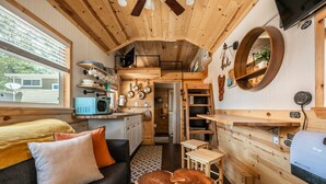 A compact, wooden interior with a kitchenette, a sofa, a dining area, and a large mirror. - Glamping Under the Stars | Firepit, BBQ & Views (Woodland Park)