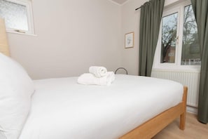 Ein ordentlich bezogenes Bett mit weißen Leinen und gerollten Handtüchern, ein Fenster mit Vorhängen und eine Heizung.