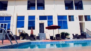 Un hotel con piscina, mobiliario exterior y una amplia fachada.