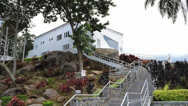A set of stone stairs leading up to a white building with a modern design, surrounded by landscaped gardens and large rocks. - Summit Resort (Ado Ekiti)