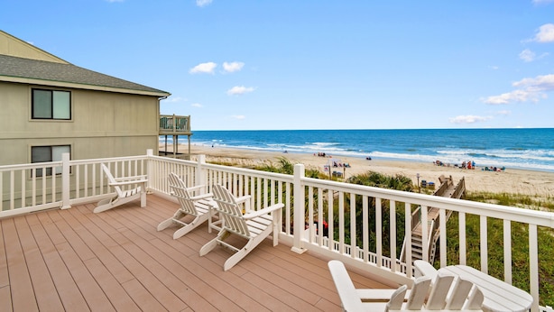 Um terraço com guarda-corpos brancos e cadeiras Adirondack, com vista para uma praia.