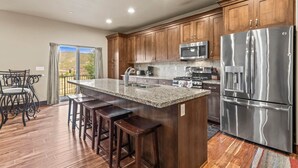 A modern kitchen with wooden cabinets, stainless steel appliances, a granite countertop, and a bar stool area.
