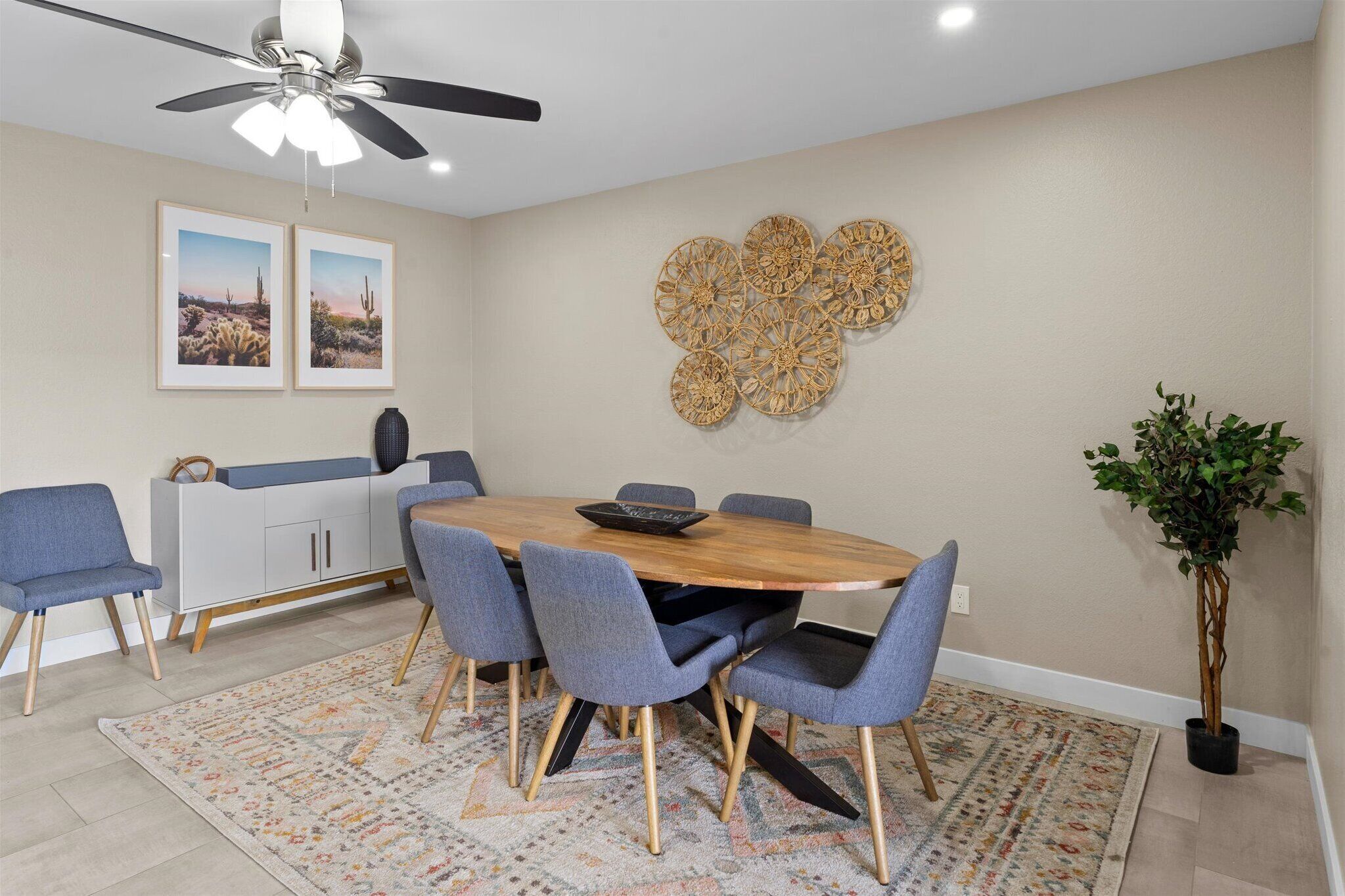 A dining area with a round table, six chairs, a ceiling fan, and a decorative wall piece.