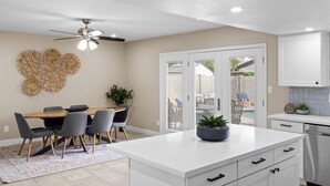 A modern kitchen with white cabinetry, a central island, and a dining area with a wooden table and chairs.