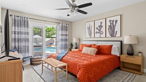 A bedroom with a bed, bedside tables, a desk, a chair, a ceiling fan, and a view of a pool through the glass door.
