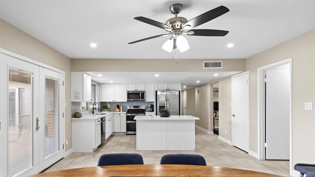 A modern kitchen with white cabinets, a central island, and a ceiling fan.