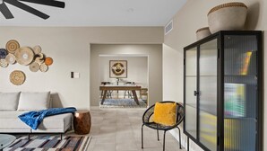 A living room with a sofa, a patterned rug, a coffee table, a cabinet, and a dining area in the background.