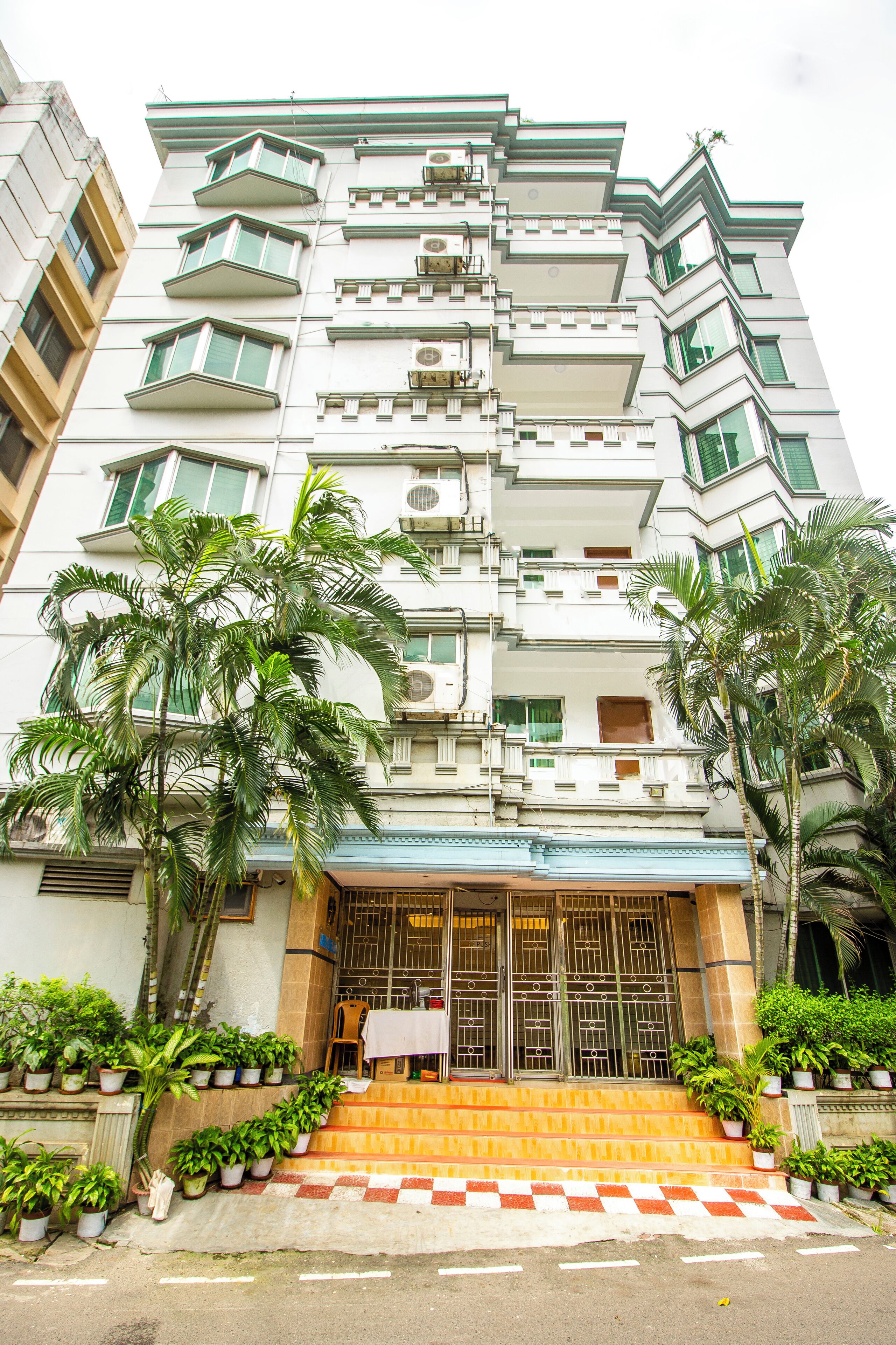A multi-story building with a central entrance, steps leading up to it, and potted plants around the entrance.