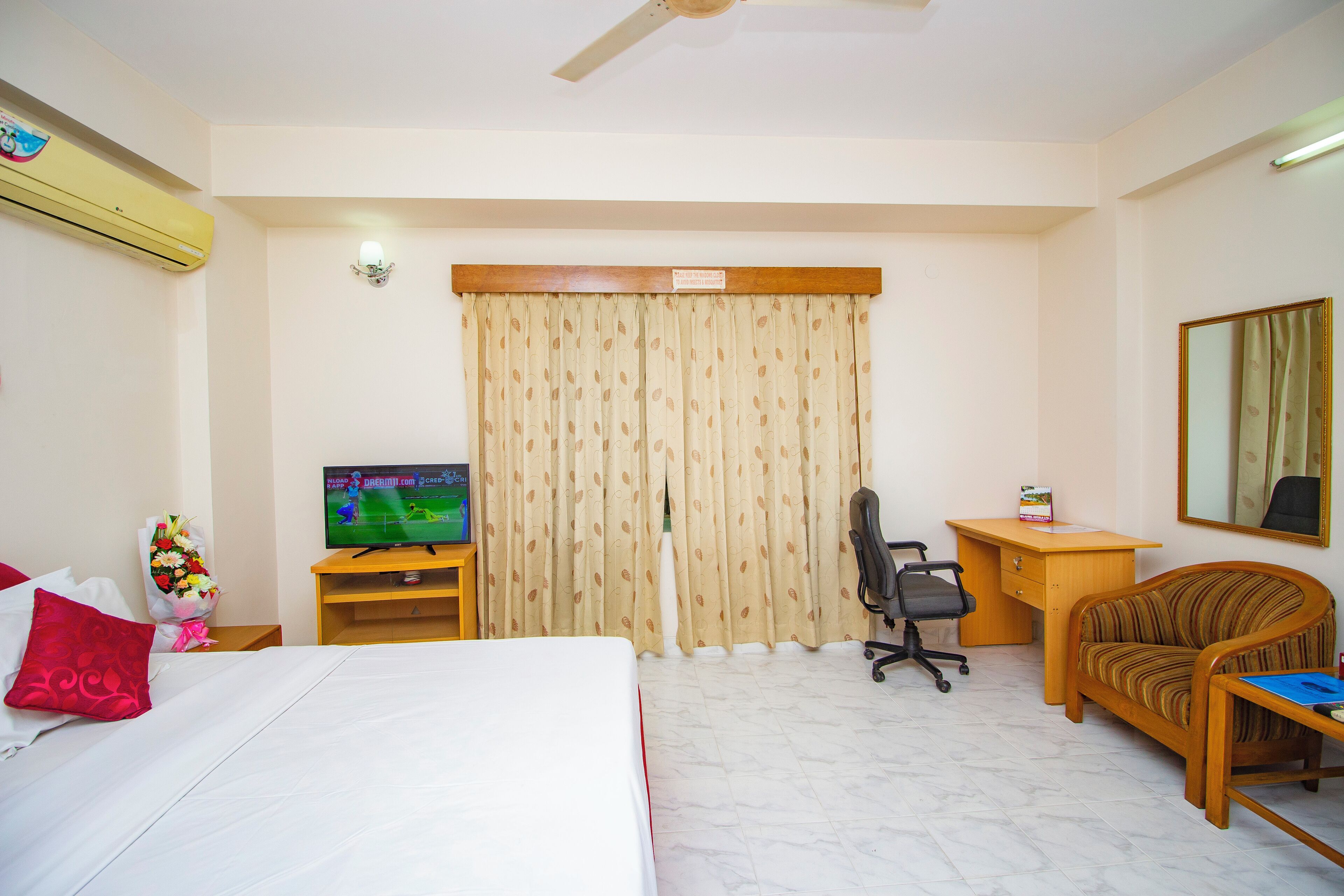Una habitación de hotel con cama, escritorio, silla, televisor y cortina.