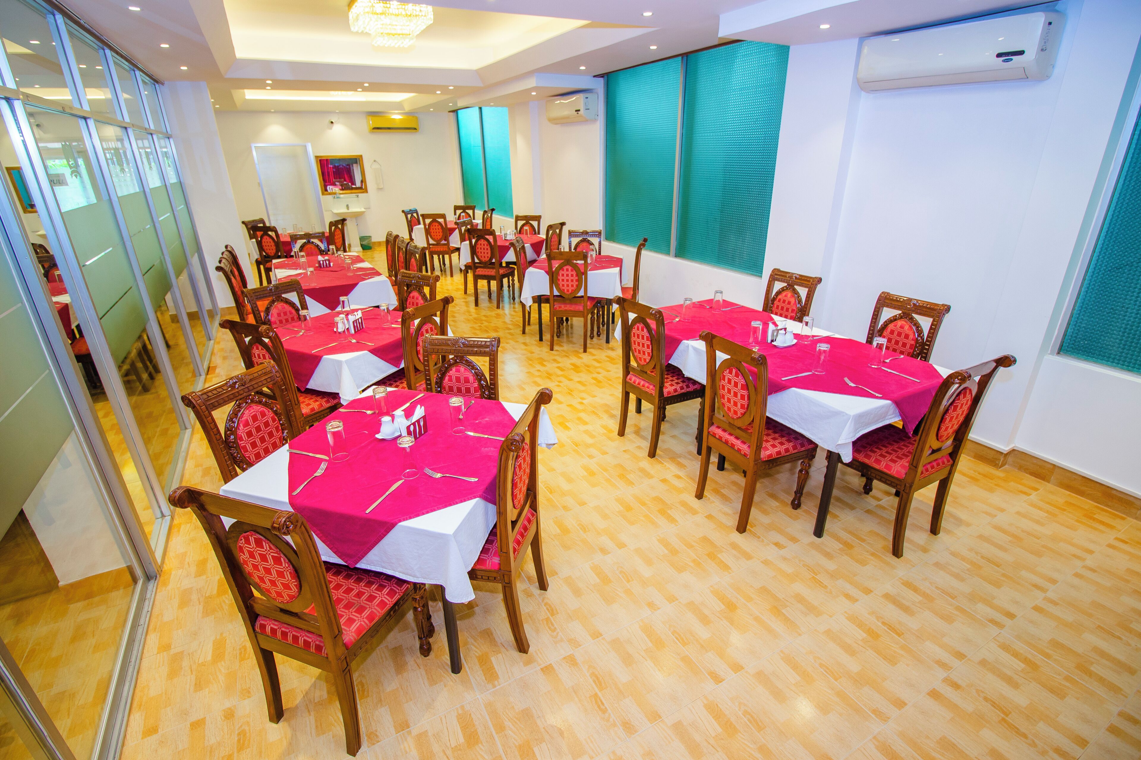 A dining area with multiple tables covered with red tablecloths and wooden chairs.