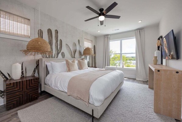 A modern bedroom with a large bed, a ceiling fan, and a view of the outdoors.