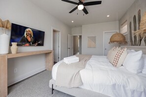 A modern bedroom with a bed, a TV mounted on the wall, a ceiling fan, and a cactus wall decoration.