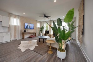 A modern living room with a television, a ceiling fan, and large plants.