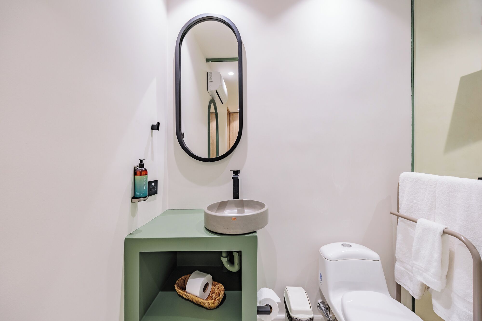 A bathroom with a round sink, a toilet, a mirror, and a towel rack.