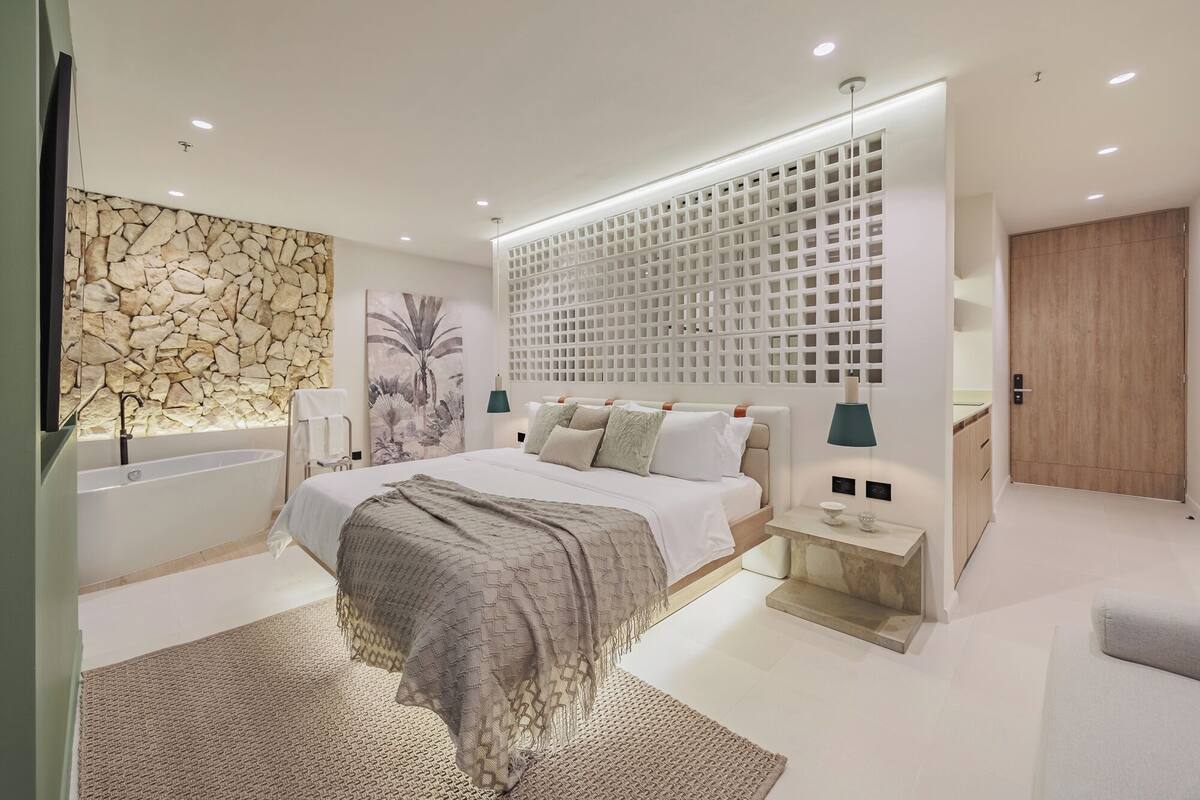 A modern bedroom with a stone wall, a large bed with a headboard, a wooden wardrobe, and a built-in shelf unit.